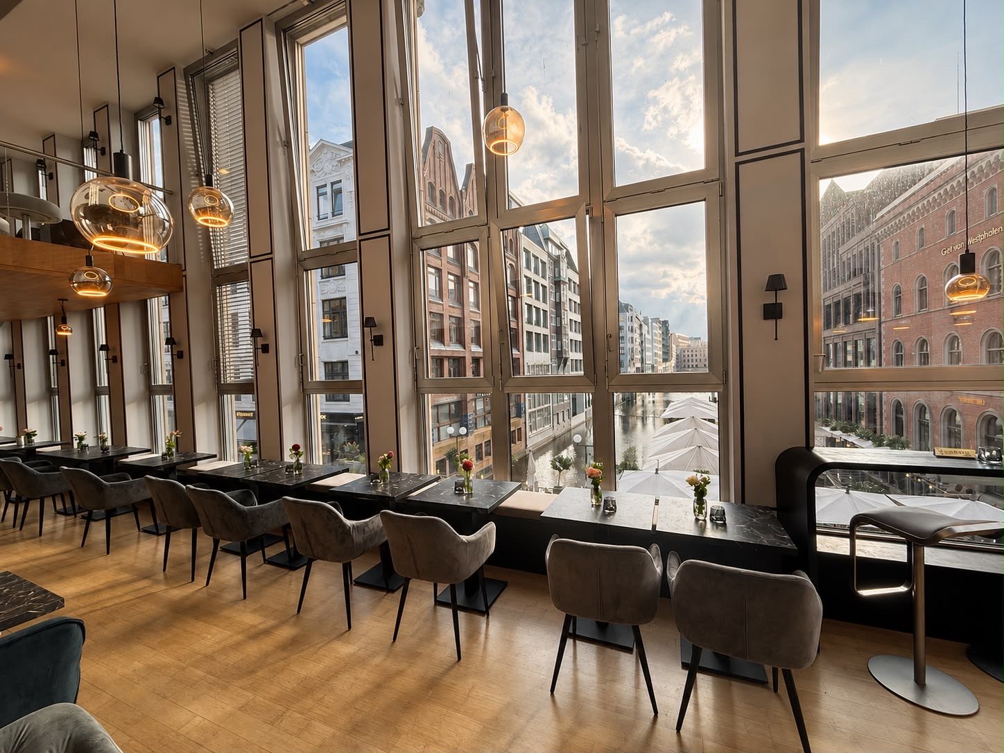Fensterfront des N6 mit Pendelleuchten, gedeckten Tischen und Blick über das Wasser
